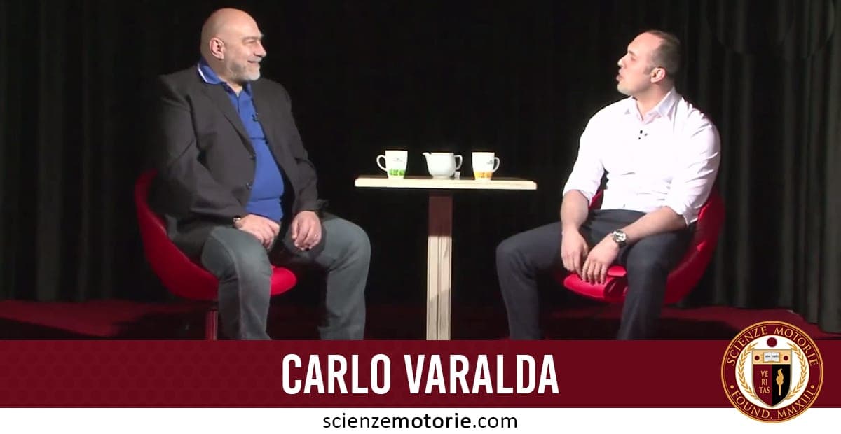 Carlo Varalda e Giacomo Catalani seduti su sedie rosse conversano davanti a un tavolino con tazze, sfondo scuro e logo Scienze Motorie in basso a destra.